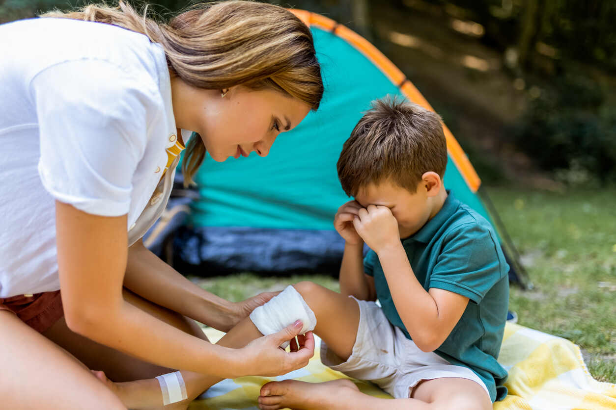 Woman treating injured child’s leg with bandage at summer camp, highlighting risks and liability issues for camp injuries.